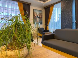A modern living room with a large potted plant, a sofa, and a painting on the wall.
