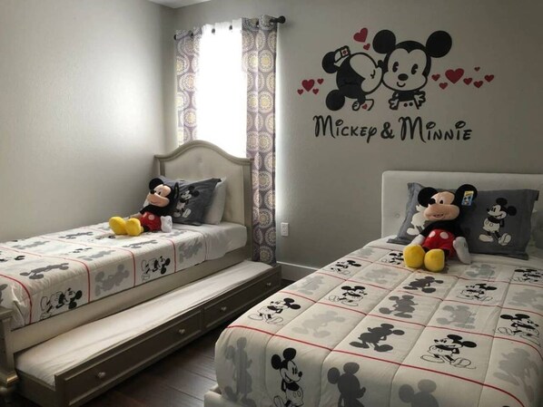 Une chambre avec deux lits, chacun agrémenté de linge de lit aux motifs de Mickey Mouse. Un autocollant mural représentant Mickey et Minnie Mouse est placé au-dessus des lits.