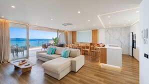 A modern living room with a sofa, dining area, kitchen, and large windows overlooking the sea. - Vistamar IV frontline sea Apt. in a prime location in Puerto Pollensa (Puerto Pollensa)