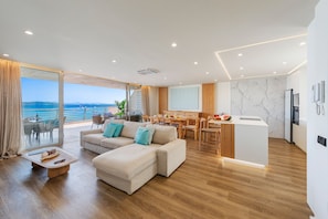 Una sala de estar moderna con sofá, comedor, cocina y ventanas grandes con vista al mar.
