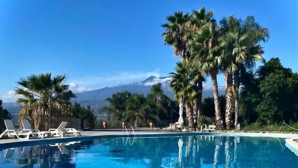 A swimming pool with clear blue water, surrounded by palm trees and lounge chairs. - Borgo San Biagio (Calatabiano)