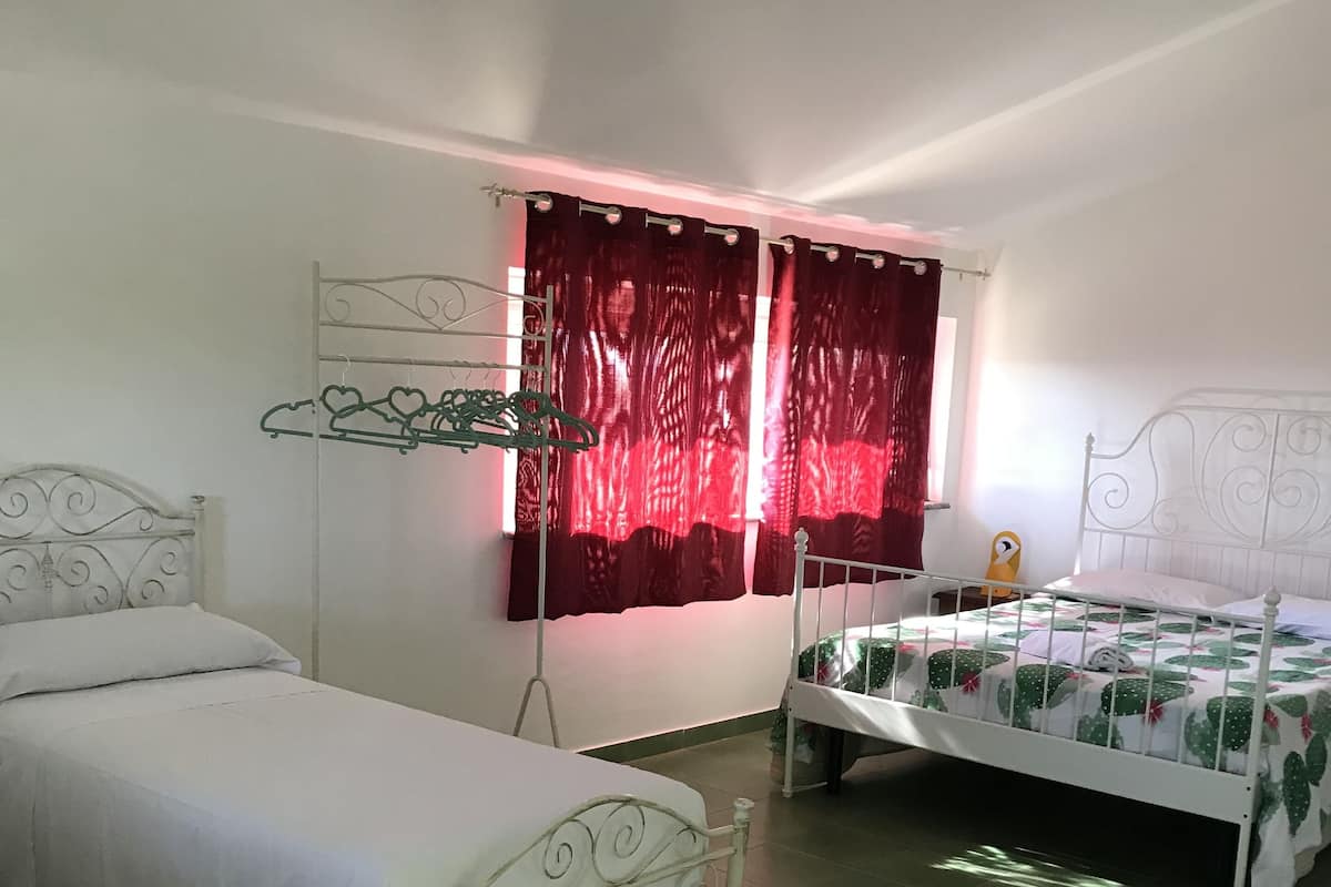A bedroom with two single beds, a metal wardrobe, and a window with red curtains.