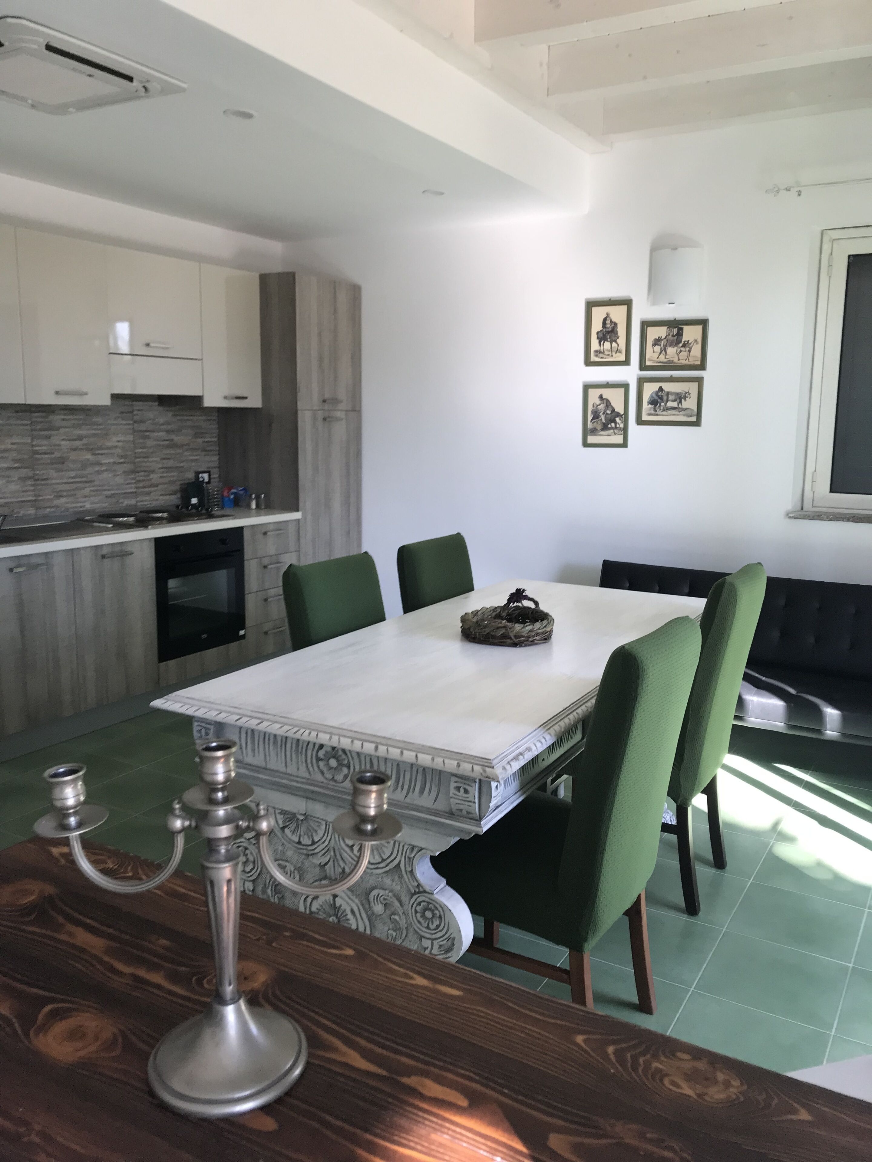 A modern kitchen with white cabinets, a built-in oven, and a dining area with a white table and green chairs.