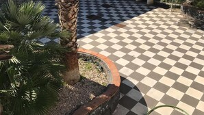 A patio with a checkered floor, surrounded by palm trees and olive trees, with a view of distant mountains. - Borgo San Biagio (Calatabiano)