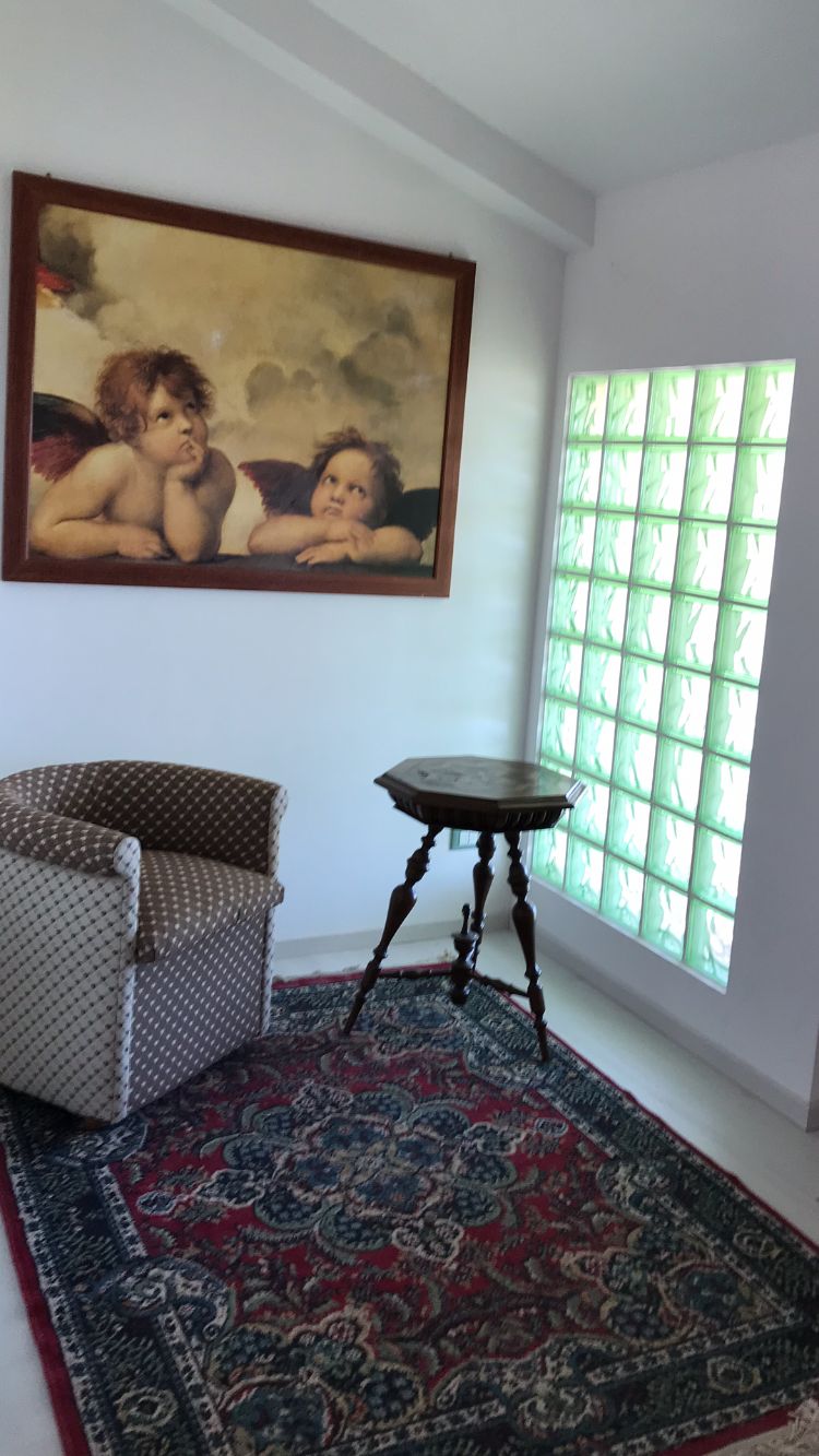 Une pièce comprenant un fauteuil à motifs, une petite table ronde, un grand tableau et un tapis à motifs.