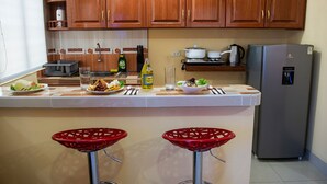 Cozinha com armários de madeira, geladeira de aço inoxidável e um espaço de bar com banquetas vermelhas.