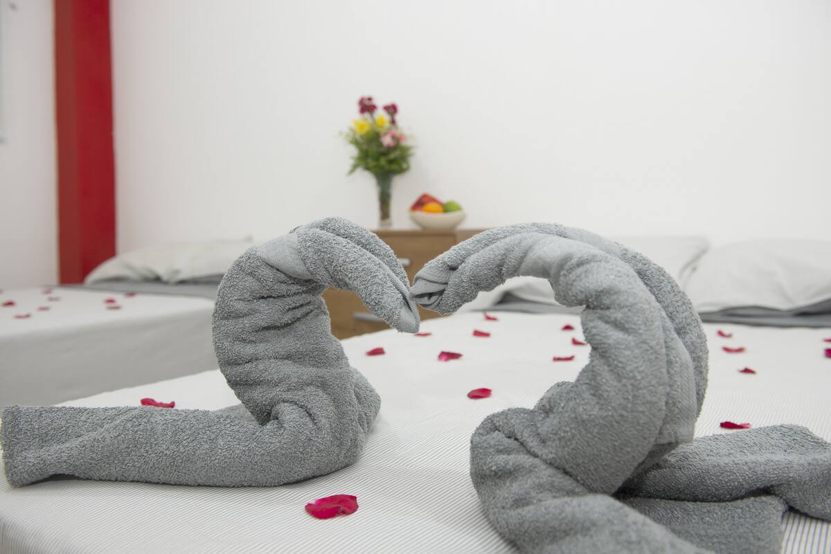 Ein Bett mit Rosenblättern und einer Handtuch-Herz-Arrangement.