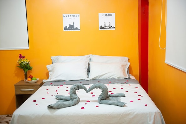 A hotel room with a bed, pillows, a nightstand with a vase of flowers, and two posters on the wall.