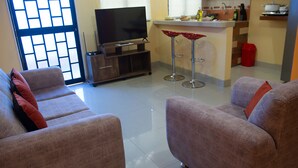 Sala de estar com sofá, televisão e área de cozinha com um banquinho.