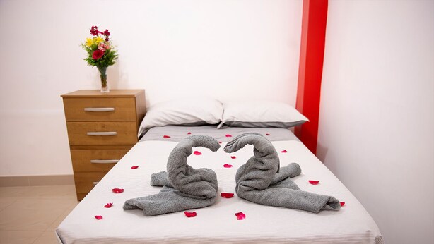 Quarto de hotel com cama, cómoda de madeira e um vaso de flores.