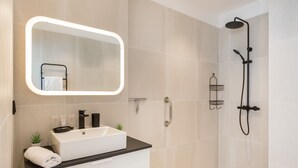 Une salle de bain moderne avec un lavabo blanc, un plan de toilette noir et un grand miroir doté d’un cadre éclairé.