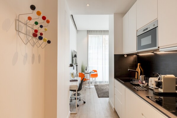 A modern kitchen with a built-in oven, a coffee maker, and a microwave. There is a dining area with a table and chairs, and a kitchen island with a sink.