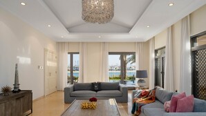 A spacious living room with a grey sofa, a wooden coffee table, and a chandelier. - Exclusive Villa w/ Private Pool, Garden & Beach (Dubai)