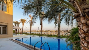 A swimming pool with clear blue water, surrounded by palm trees and a view of a city skyline. - Exclusive Villa w/ Private Pool, Garden & Beach (Dubai)