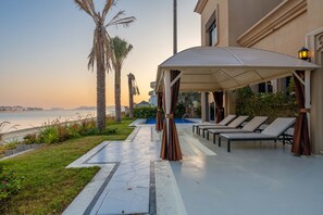 A covered outdoor area with lounge chairs and a pool, overlooking a body of water.
