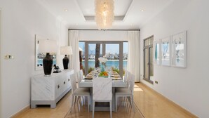 A dining area with a view of a cityscape through large windows, a marble console table, and a chandelier. - Exclusive Villa w/ Private Pool, Garden & Beach (Dubai)