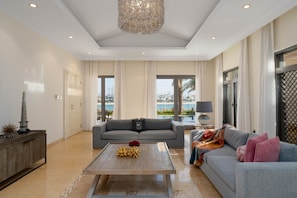 A spacious living room with a grey sofa, a wooden coffee table, and a chandelier.