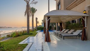 A covered outdoor area with lounge chairs and a pool, overlooking a body of water. - Exclusive Villa w/ Private Pool, Garden & Beach (Dubai)