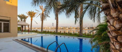 A swimming pool with clear blue water, surrounded by palm trees and a view of a city skyline.