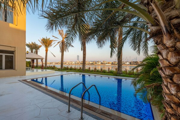 A swimming pool with clear blue water, surrounded by palm trees and a view of a city skyline.