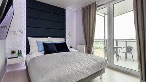 Ein modernes Schlafzimmer mit einem großen Bett, weißen Ziegelwänden, einem dunklen Kopfteil und einem Balkon mit Sitzgelegenheit.