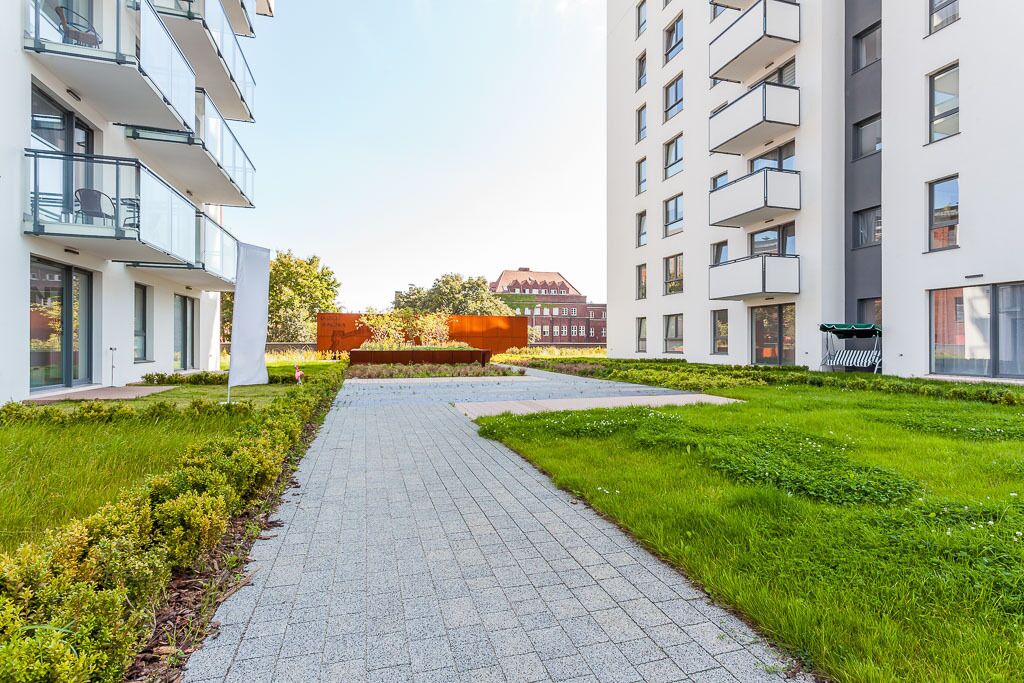 Un moderno complejo de apartamentos con un sendero central, césped verde y una estructura roja al fondo.