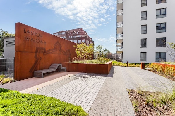 A modern building with a sign reading "Bastion Walowa" and a paved courtyard with steps leading to a seating area.