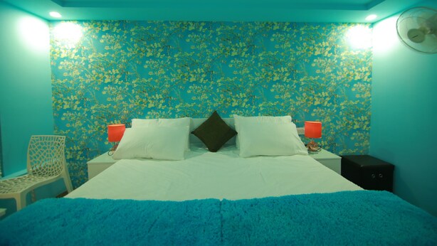 A bedroom with a floral wallpaper, a bed with white and blue bedding, two bedside lamps, a nightstand, a chair, and a ceiling fan. - Best Kerala Houseboat (Ambalapuzha)