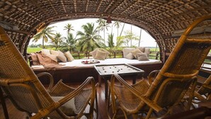 A cozy, open-air seating area with wicker furniture and a view of palm trees. - Best Kerala Houseboat (Ambalapuzha)