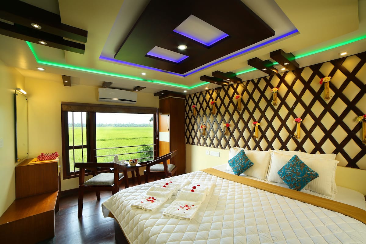 A hotel room with a large bed, a balcony with a view of the countryside, and a modern ceiling design with recessed lighting.