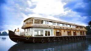 Een ruime woonboot met meerdere dekken en ramen, drijvend op kalm water.
