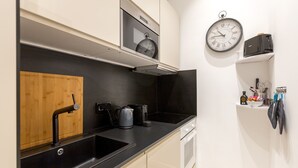 Eine moderne Küche mit schwarzem Arbeitsplatz, Schneidebrett, Kaffeemaschine und einer Uhr an der Wand.