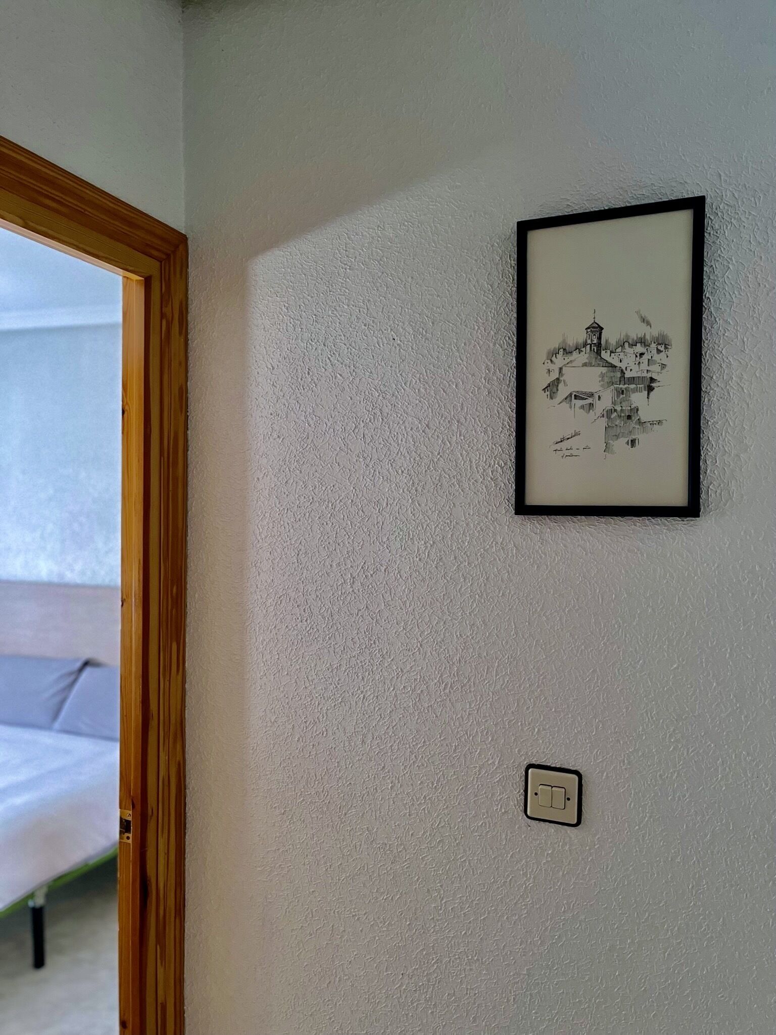 Ein Zimmer mit einer Wand mit Strukturmuster, einer gerahmten Schwarz-Weiß-Zeichnung und einem Lichtschalter.