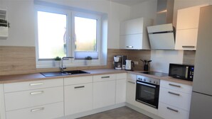A modern kitchen with white cabinets, a built-in oven, a microwave, and a coffee maker. - Hello and welcome to the Deichtraum! (Dangast)
