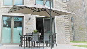 An outdoor patio with a table and chairs, a large umbrella, and a building with a brick facade in the background. - Hello and welcome to the Deichtraum! (Dangast)