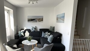 A modern living room with a black sectional sofa, two grey armchairs, a round white coffee table, and a small potted plant. - Hello and welcome to the Deichtraum! (Dangast)