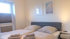 A neatly made bed with two pillows and folded towels, a bedside table with a remote control, and two framed pictures on the wall. - Hello and welcome to the Deichtraum! (Dangast)