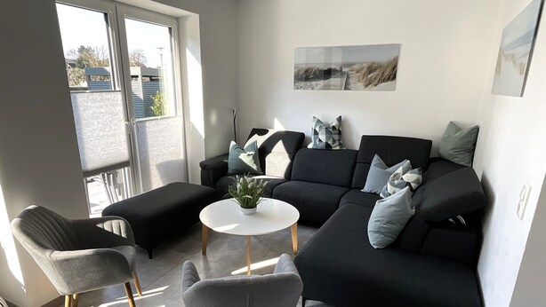 A modern living room with a black sofa, two grey armchairs, a small white table, and a potted plant. - Hello and welcome to the Deichtraum! (Dangast)