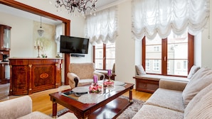A living room with a wooden coffee table, patterned sofas, a television, and a chandelier. - Frey Homes Gdansk Old Town (Gdansk)