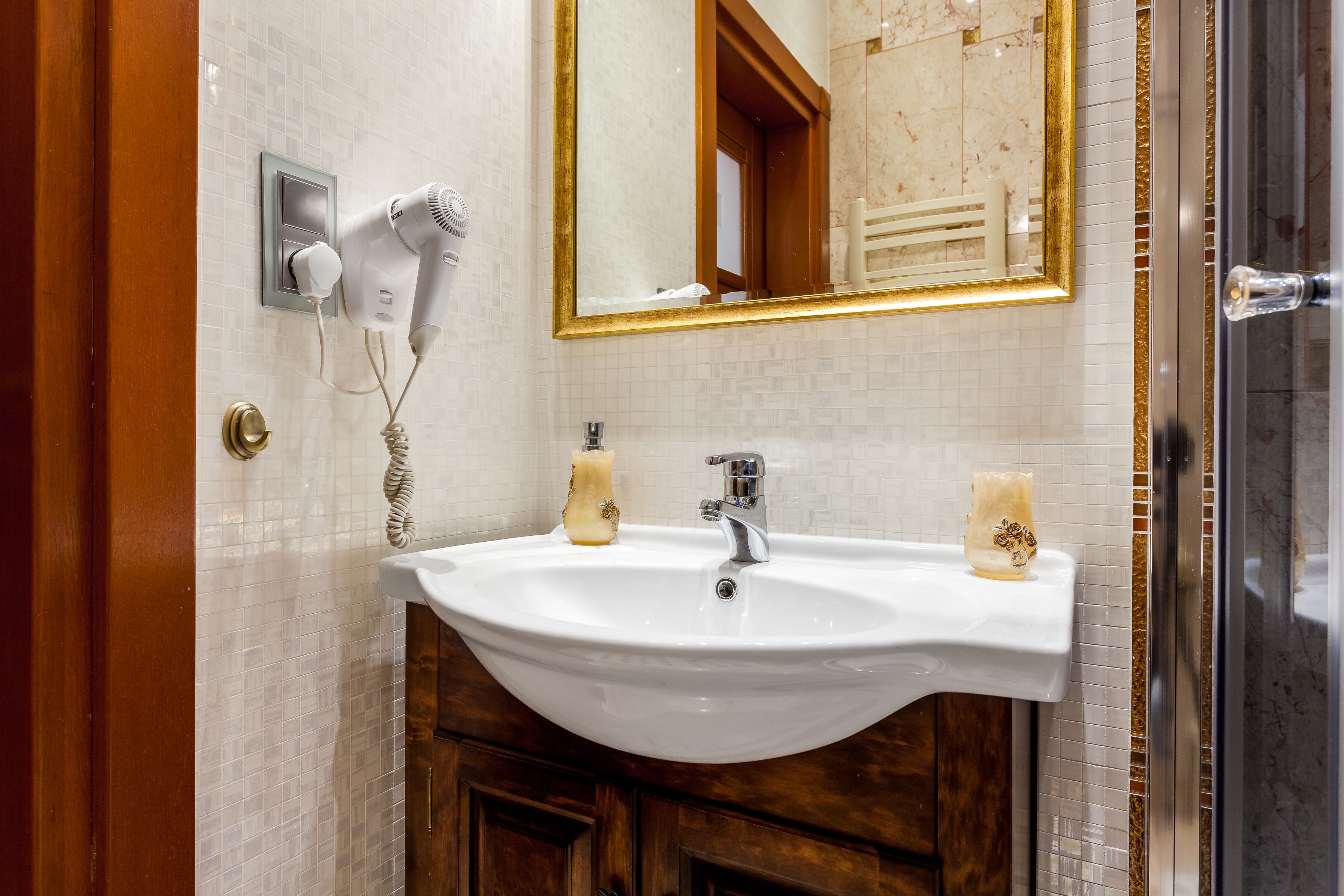 A bathroom with a white sink, a mirror with a gold frame, and a hairdryer on the wall.