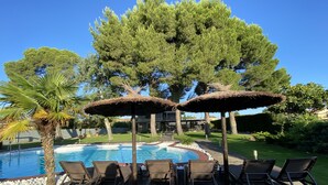 A poolside area with lounge chairs and thatched umbrellas, surrounded by trees and a clear blue sky. - Luxury villa with detail decorated pool (Zaragoza)