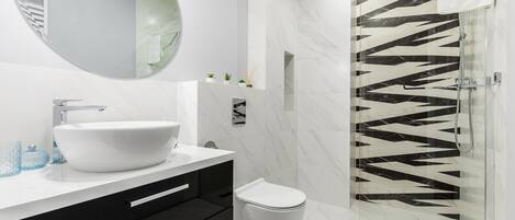 A modern bathroom with a white sink, black cabinets, a toilet, and a glass shower enclosure with a black and white tile pattern.