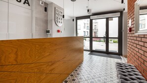 A reception area with a wooden reception desk, a patterned floor, and a brick wall. - Frey Homes Superior Old Town (Gdansk)