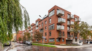 A multi-story residential building with balconies, a parking sign, and a wet street reflecting the surroundings. - Frey Homes Superior Old Town (Gdansk)