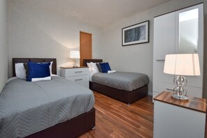 A hotel room with two beds, a nightstand with a lamp, a wardrobe, and a framed picture on the wall. - Oldbrook House (Milton Keynes)