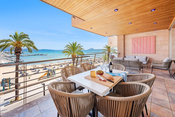 A terrace with wicker furniture, a table with food, and a view of the beach and sea.