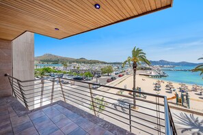 A balcony with a view of a beach, a parking area, and a mountainous landscape.