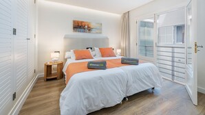 A double bed with white bedding and orange pillows, a bedside table with a lamp, a painting on the wall, and a sliding glass door. - Vistamar II frontline sea Apt. in a prime location in Puerto Pollensa (Puerto Pollensa)
