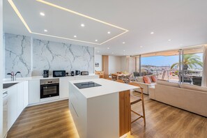 A modern kitchen with a marble backsplash, wooden flooring, and a dining area with a view.
