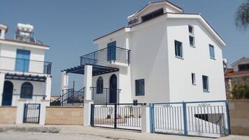 Un edificio de dos pisos con fachada blanca, contraventanas azules y un balcón.